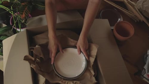 Prepare for a Move Woman Wrapping Ceramic Plates in Brown Paper
