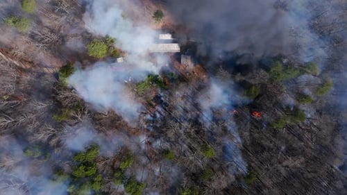 Top down aerial footage of a house in the forest with a wildfire burning all around it.