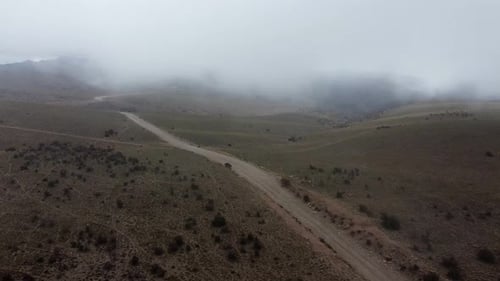 Low cloud aerial follows gravel road on foggy mountain plateau, Andes