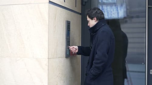 Teenage boy chatting on intercom system at modern apartment building entrance