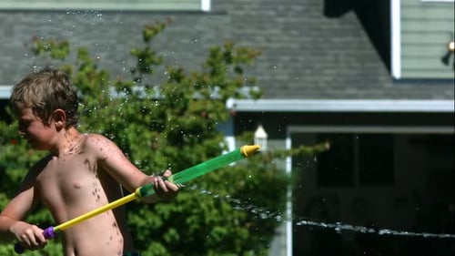 Boy squirts water from squirt gun in yard