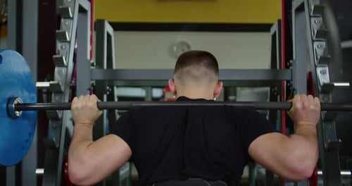 Muscular Athletic Man Squatting with a Barbell in the Gym