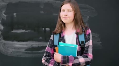Smiling Schoolgirl with Backpack Stands by Blackboard