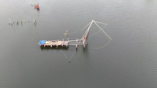 Imagens de drones capturam a estrutura tradicional da rede de pesca chinesa que se estende sobre um verde acinzentado calmo
