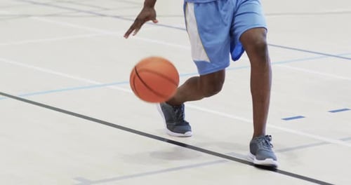 Mittelteil eines afroamerikanischen männlichen Basketballspielers, der auf dem Hallenplatz Ball hüpft, Zeitlupe