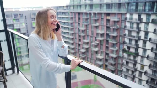 Woman Laughing on Smartphone on Urban Apartment Balcony