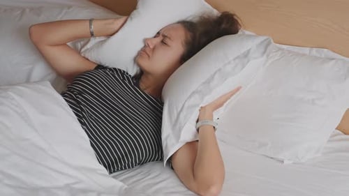 Woman in Bed Covers Ears with Pillow