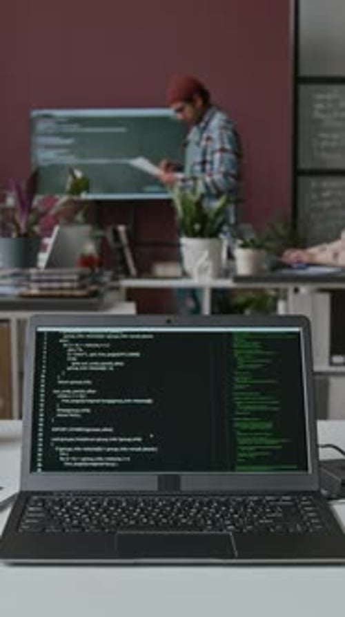 Timelapse of Laptop with Running Lines of Code on Desk at Busy IT Startup