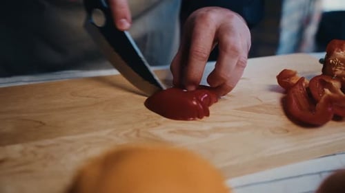 Close-up of hands slicing a red bell pepper on a wooden cutting board with a sharp knife