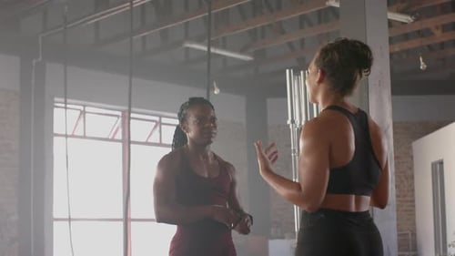 Discussing workout routine, two women in gym wearing athletic clothing