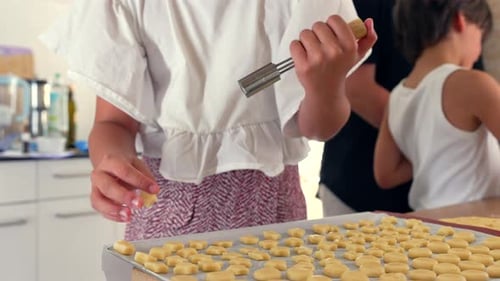 Young girl pressing dough on a baking tray with focused attention, while a boy shapes dough beside