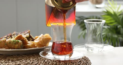 Woman pouring Turkish tea into glass cups at table, closeup