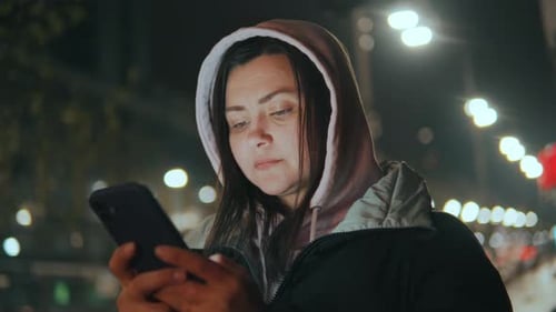 Woman Uses Smartphone at Night in the City