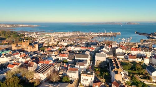 Slow high forwards drone footage of the roof tops of St Peter Port Guernsey in the golden hour with