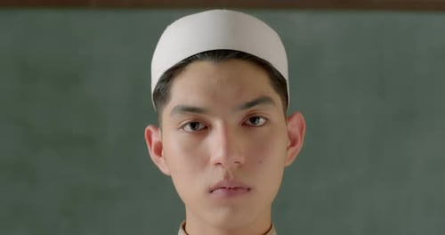 A handsome Asian high school boy who is a Muslim wearing a white Islamic prayer cap