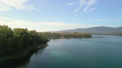 malerische Landschaft mit einem riesigen See, umgeben von üppigem Grün und bewaldeten Hügeln. Der See ist ruhig