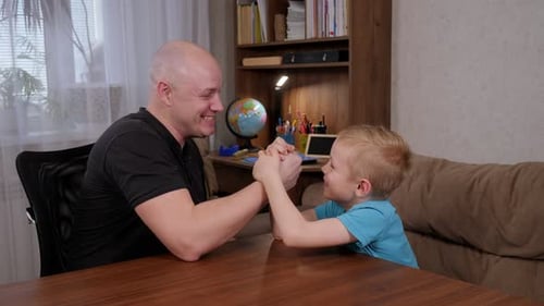 Father and Son Arm Wrestling at Table