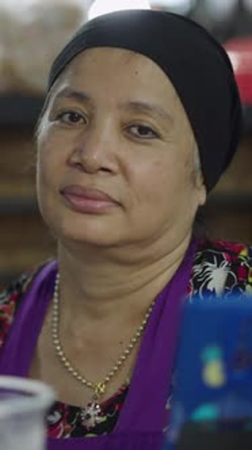 Retrato de uma mulher asiática madura olhando para a câmera enquanto espera ser servida em um mercado local