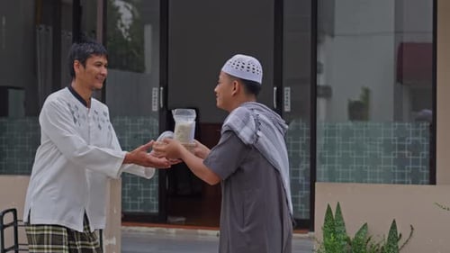 Muslim man hands giving rice zakat to neighbor at mosque practicing Zakat Al-Fitr charity