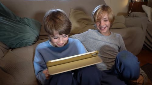 Two Boys Enjoying a Tablet Indoors on Sofa