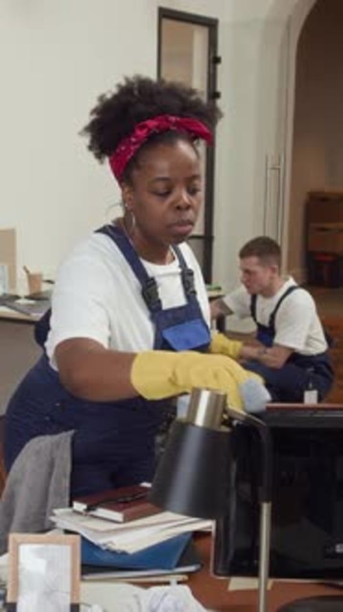 Female Janitor Wiping Computer during Office Cleanup with Team