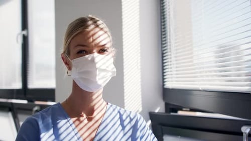 Blond Woman in Mask Looks Out Bright Window