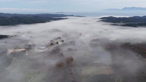 Panoramic aerial drone shot of a vast foggy valley with farmland and scattered houses surrounded by