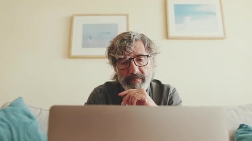 Close up, elderly man working on laptop sitting on the sofa in the living room