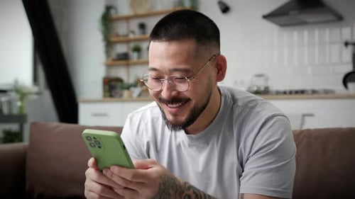 Adult Man Laughing While Using Smartphone at Home