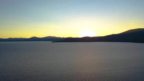 Sun Rising Over Lake with Mountains Silhouette in Background. Bright Yellow Sun with Golden Glow Ref