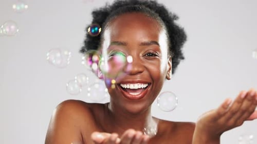 Face, skincare and laughing black woman with bubbles in studio isolated on gray background