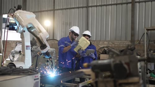 Blue collar workers at machine shop with welding robot arm.