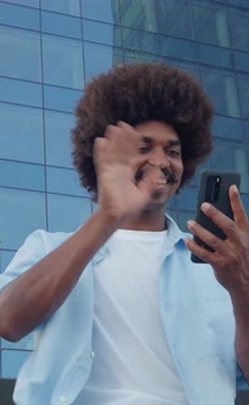 Man Smiles, Waves, Using Mobile Phone in City