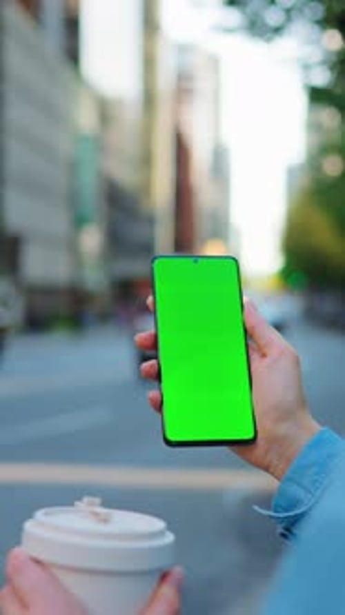 Una mujer está parada en la calle y usa un teléfono inteligente con pantalla verde