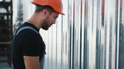 Gestresster Mitarbeiter mit orangefarbenem Schutzhelm schlägt seinen Kopf gegen den Zaun