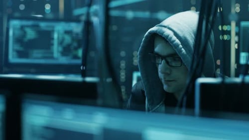 Man in Hoodie Working at Multiple Computer Screens