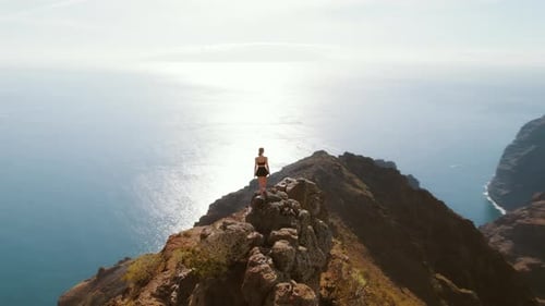 Person stands on cliff edge in Tenerife, overlooking the shimmering sea. Ocean view and rugged coast