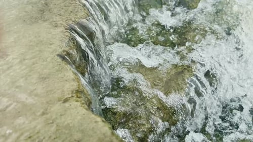 a close-up dynamic view of water flowing and cascading over a series of textured moss-covered