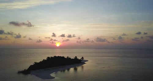 Aerial view of a desert island on sunset with a clear and transparent sea and a pristine beach.