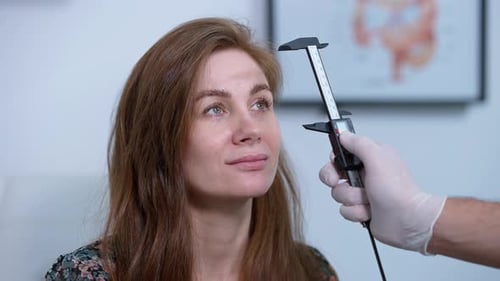 Gros plan d'une femme caucasienne positive regardant un médecin méconnaissable mesurant le visage avec Vernier