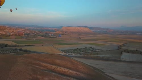 Drone shot of hot air balloons flying over a mountain landscape, Cappadocia, Turkey, on a sunny even