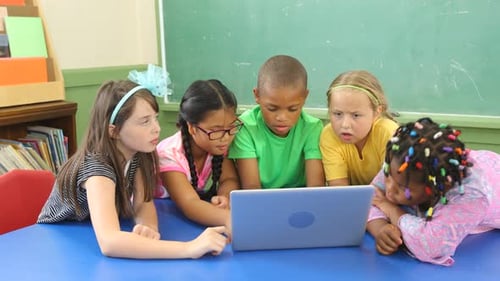 Kids smiling learning together on laptops in a bright elementary school classroom