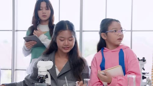 Schoolgirl and friends in classroom Trying out microscope during elementary school science lesson,