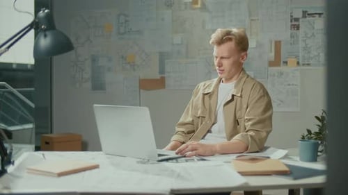 Konzentrierter junger Architekt tippt auf Laptop und forscht im Büro