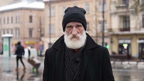 An Elderly Man Dressed in a Warm Winter Coat Stands on a City Street Surrounded By Urban Scenery
