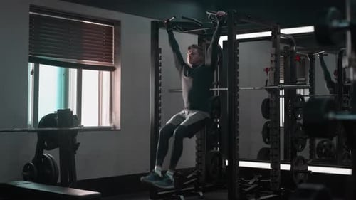 Strong athletic caucasian man doing hanging knee raises, working out on horizontal bar in a fitness