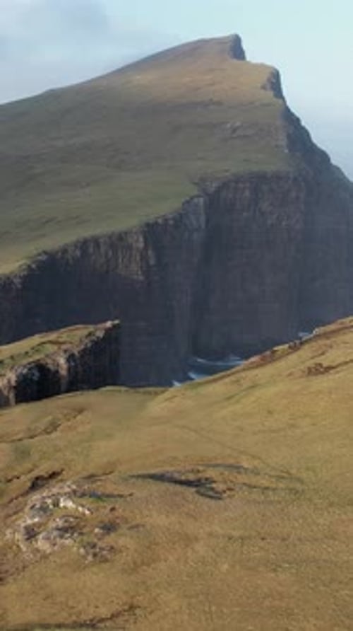 Stunning aerial view flying over green hills and dramatic cliffs with waves crashing against the