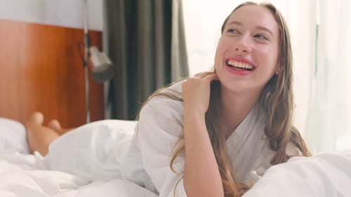 Smiling Woman Relaxing in Bed Wearing White Robe
