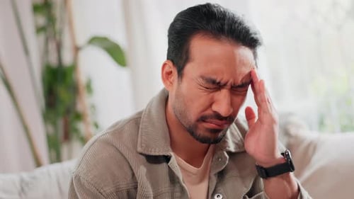 Asian man, headache and stress with vertigo on sofa for pain, dizziness or illness at home