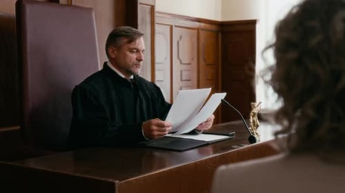 Unrecognizable Woman Listening to Judge Reading Document in Courtroom